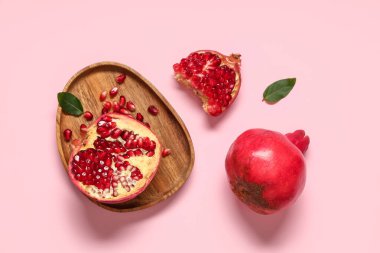 Tahta tepsi taze olgun nar ve pembe arka planda tohumlar.