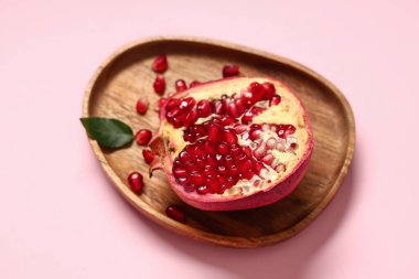 Tahta tepside taze olgun nar ve pembe arka planda tohumlar var.