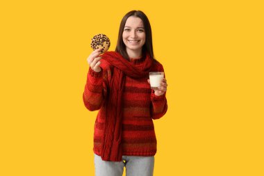 Sarı arka planda bir bardak süt ve lezzetli kurabiyeyle güzel bir genç kadın.