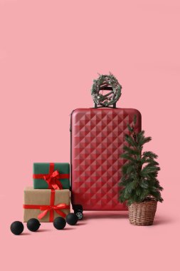 İçinde Noel ağacı olan bavul, pembe arka planda hediyeler ve toplar