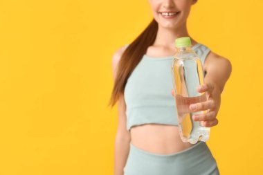 Sarı arka planda bir şişe suyu olan güzel, genç, sportif, mutlu bir kadın. Yakın plan.