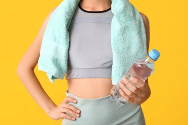 Sarı arka planda bir şişe su ve havlusu olan genç ve güzel bir kadın. Yakın plan.