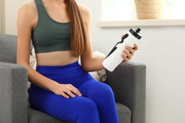 Evdeki koltukta oturan, su dolu bir şişeyle genç ve güzel bir bayan.