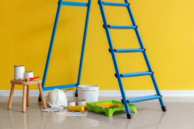 Sarı duvarın yanında boya ve aletlerle dolu bir merdiven.