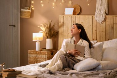 Güzel, genç ve mutlu bir kadın, elinde kitapla akşamları yatakta oturuyor.