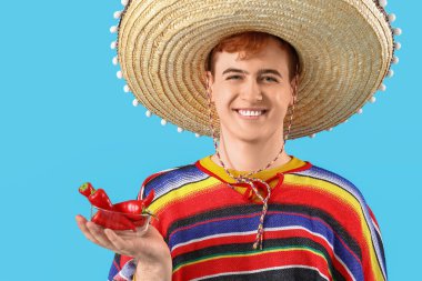 Sombrero giymiş genç Meksikalı bir adamın portresi ve mavi arka planda kırmızı biberli.