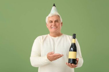 Parti şapkalı son sınıf öğrencisi yeşil arka planda bir şişe şampanyayla Noel 'i kutluyor.