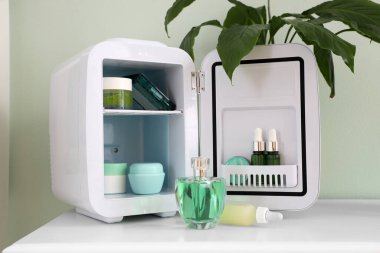 Küçük buzdolabı ve kozmetik ürünleri ışık duvarının yanındaki masada.