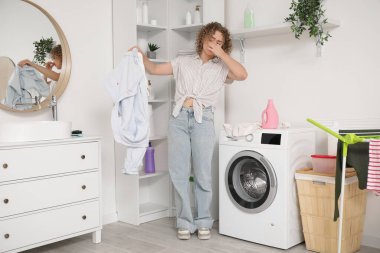 Çamaşırhanede kokuşmuş giysileri olan hoşnutsuz genç bir kadın.