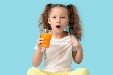 Şok olmuş küçük kız mavi arka planda tişörte meyve suyu döktü.