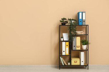 Shelf unit with document folders and plants near beige wall in office clipart