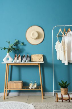 Ayakkabılar masada ve askıda, mavi duvarın yanında giysiler var.