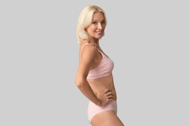 Güzel, olgun, mutlu, gri arka planda iç çamaşırlı pozitif kadın.