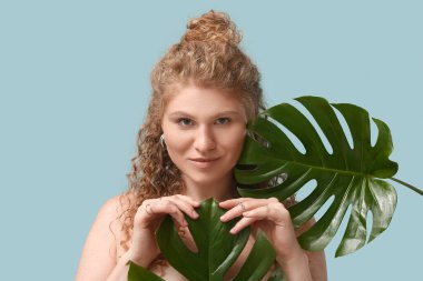 Mavi arka planda tropikal canavar yaprakları olan güzel genç bir kadın.
