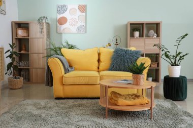 Rahat bir kanepe, oturma odasının iç tarafında ev bitkisi ve dergi olan bir sehpa.