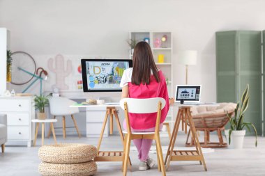 Young female graphic designer working at table in office, back view