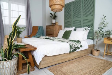 Konforlu yatağı, çiçekleri ve yeşil kıvrımlı perdesi olan aydınlık yatak odasının içi