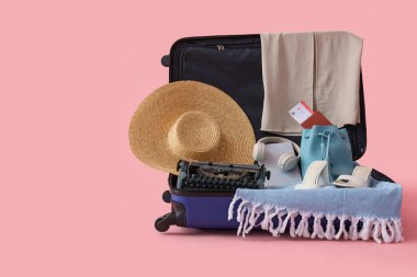 Klasik daktilo ve pembe arka planda giysileri olan bavulu aç