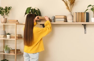 Genç bir kadın kitaplarını raftan odaya götürüyor.