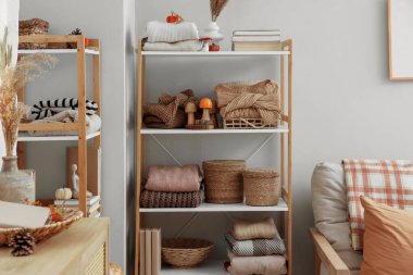 Oturma odasındaki bej duvarın yanında şık kıyafetler ve sonbahar süslemeleri olan raflar.