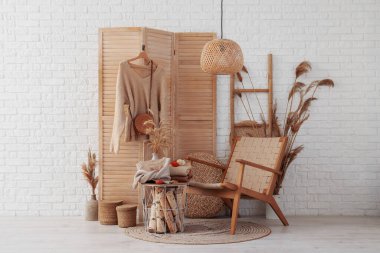 Masada şık kıyafetler ve sonbahar dekorasyonları ve beyaz tuğla duvarın yanında katlanır ekran var.