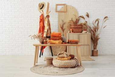 Soyunma odasındaki beyaz tuğladan duvarın yanında askılı masalarda şık kıyafetler ve sonbahar süslemeleri var.