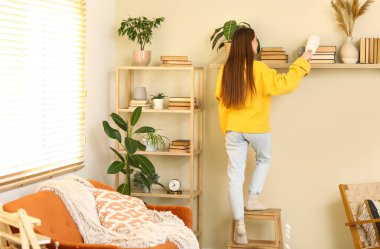 Evdeki kitap raflarındaki tozları temizleyen genç bir kadın.