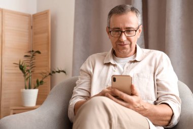 Cep telefonlu yaşlı adam evdeki koltukta oturuyor.