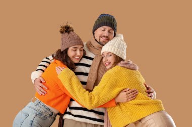 Man and two beautiful women in autumn clothes hugging on beige background. Polyamory concept clipart