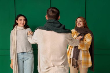 Sonbahar elbiseli iki erkek ve iki güzel kadın yeşil arka planda el ele tutuşuyorlar. Poliyamory konsepti