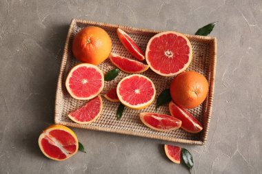 Taze greyfurtlu hasır tepsi ve gri arka planda yapraklar