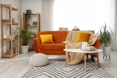 Oturma odasının içinde kırmızı kanepe, masa ve raf üniteleri var.