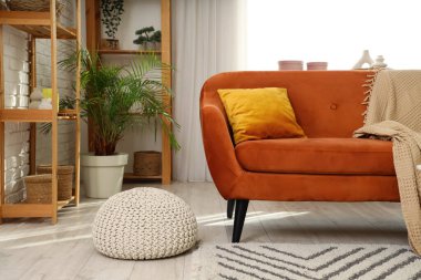 Oturma odasının içinde kırmızı kanepe, palmiye ağacı ve raf üniteleri var.