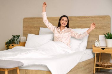 Pijamalı genç bir kadın evde yatakta uyanıyor.