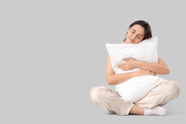 Yastıklı pijamalı genç bir kadın açık arka planda oturuyor.