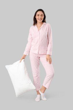 Çizgili pijamalı genç bir kadın. Arka planda yastık var.