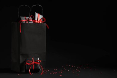 İçinde hediye kutuları ve karanlık arka planda konfeti olan bir alışveriş çantası. Kara Cuma indirimi