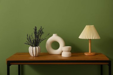 Üzerinde lavanta çiçekleri, dekor ve lamba olan vazo yeşil duvarın yanında.