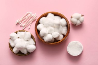 Pamuklu tahta kaseler, pamuklu çubuklar, tamponlar ve pembe arka planda çiçekler.