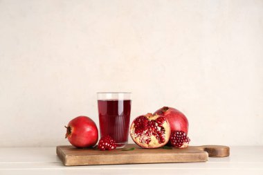 Bir bardak taze nar suyu ve beyaz ahşap masada meyveli kesme tahtası.