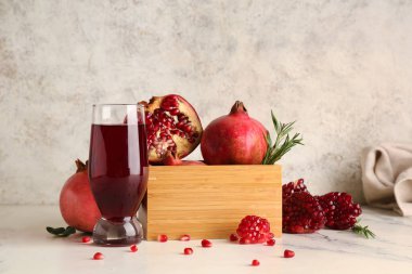 Bir bardak taze nar suyu ve beyaz arka planda meyveler olan ahşap kutu.