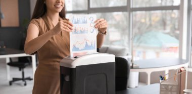 Genç sekreter ofiste kağıt öğütücü kullanarak belgeleri yok ediyor.