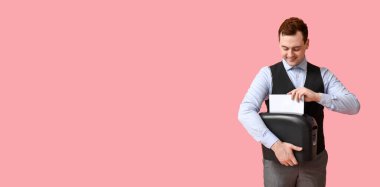 Genç erkek ofis çalışanı kağıt kâğıtlarını kağıt öğütücüsünde yok ediyor. Pembe arka planda, mesaj için yeri var.