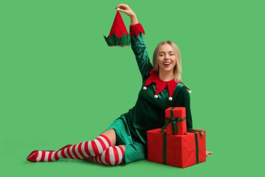 Yeşil arka planda Noel hediyesi kutuları olan elf kostümlü güzel bir genç kadın.
