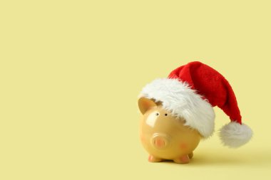 Sarı arka planda Noel Baba şapkası olan domuz kumbarası
