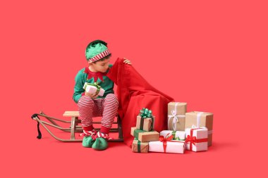 Kızağı ve kırmızı arka planda Noel hediyeleri olan şirin bir elf.