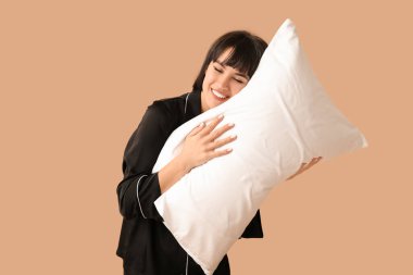 Kahverengi arka planda yumuşak yastıklı pijamalı güzel bir kadın.