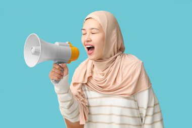 Genç Asyalı Müslüman kadın mavi arka planda megafona bağırıyor. Ulusal Duyulma Günü