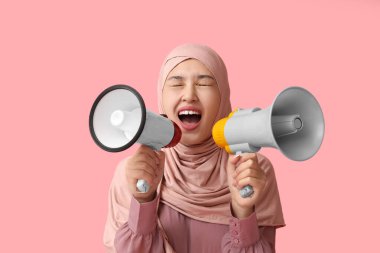 Genç Asyalı Müslüman kadın pembe arka planda megafonlara bağırıyor. Ulusal Duyulma Günü