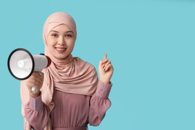 Mavi arka plandaki bir şeyi işaret eden megafonlu genç Asyalı Müslüman kadın. Ulusal Duyulma Günü